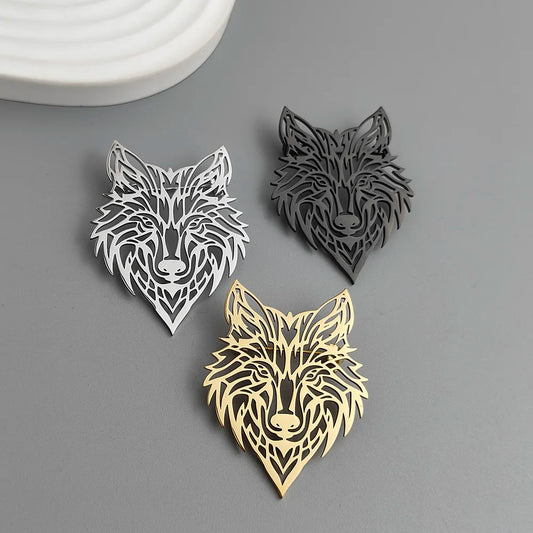Three metallic wolf head brooches / pins in silver, black, and gold on a gray background.