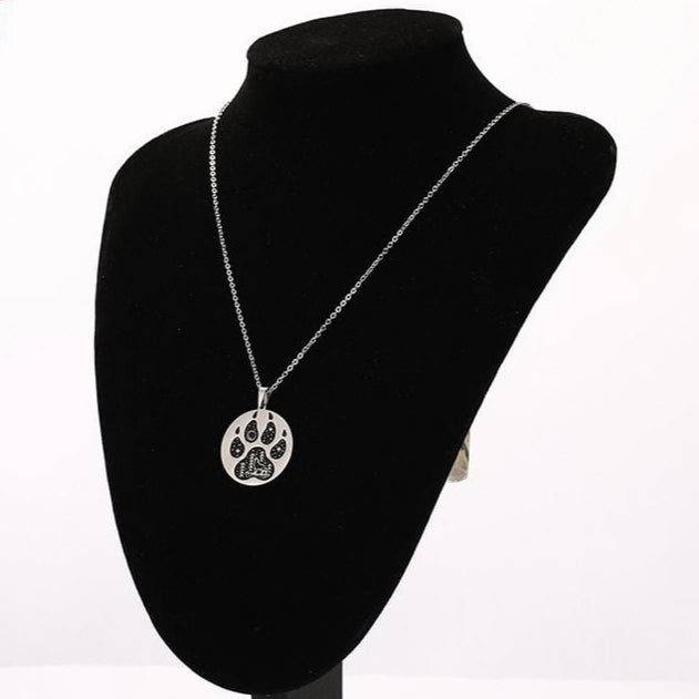 Silver necklace with a paw print pendant on a black bust against a white background
