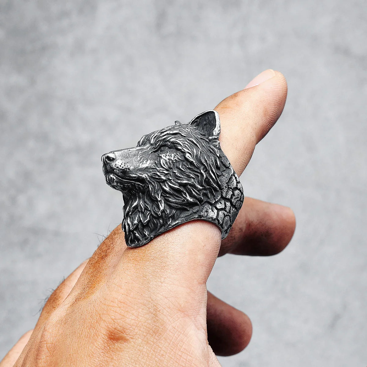 Silver wolf head ring on a finger against a gray background