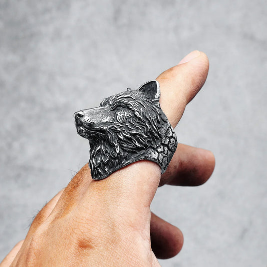 Silver wolf head ring on a finger against a gray background