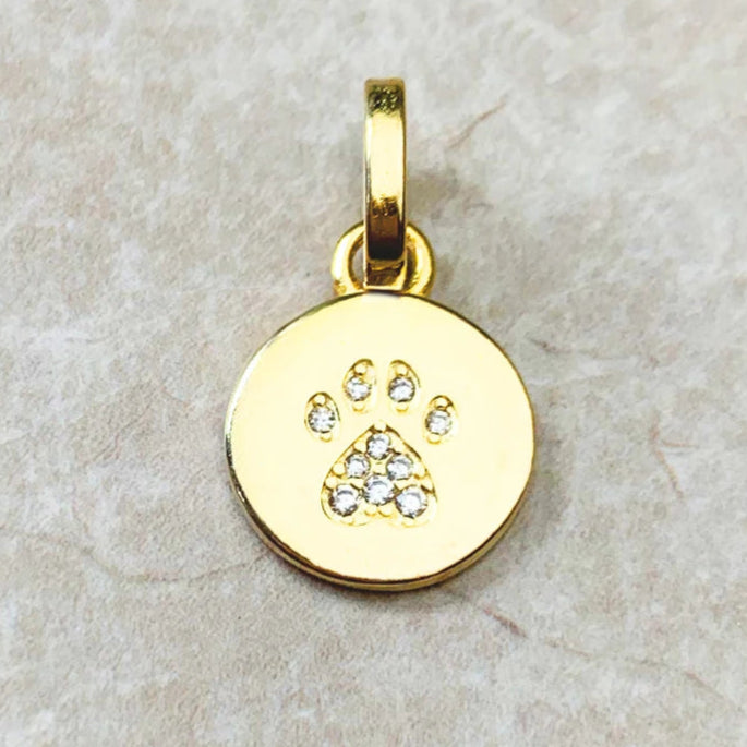 Gold pendant with paw print design on a beige stone surface