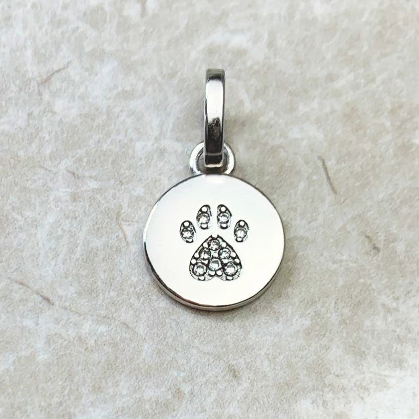 Silver pendant with paw print design on a textured beige background.