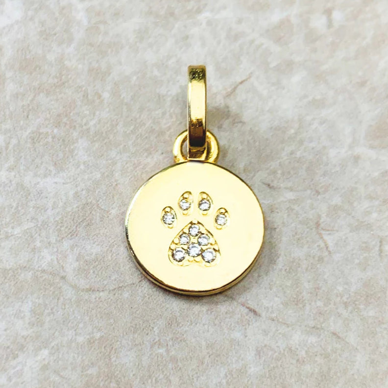 Gold pendant with paw print design on a beige stone surface.