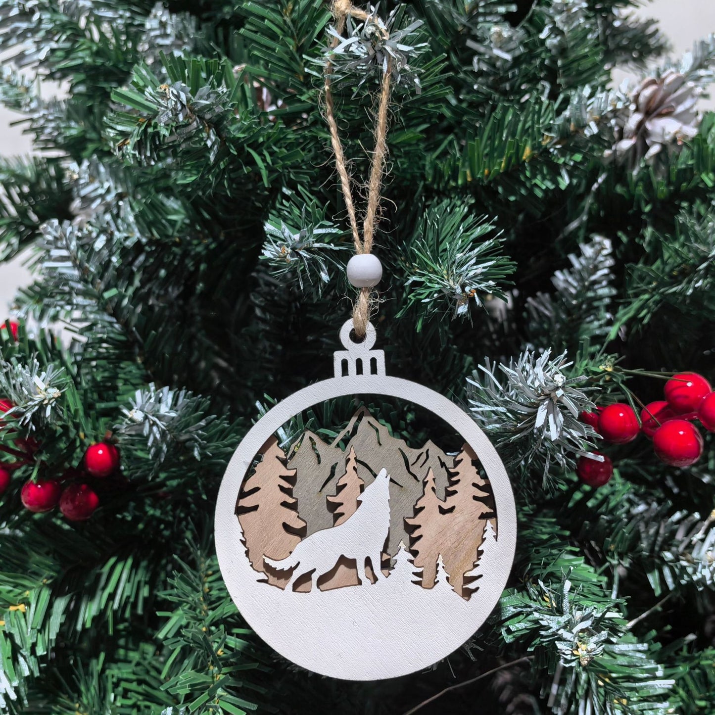 Decorative Christmas ornament with a wolf and mountain design hanging on a tree.