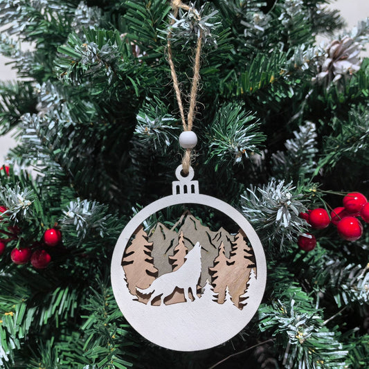 Decorative Christmas ornament with a wolf and mountain design hanging on a tree.