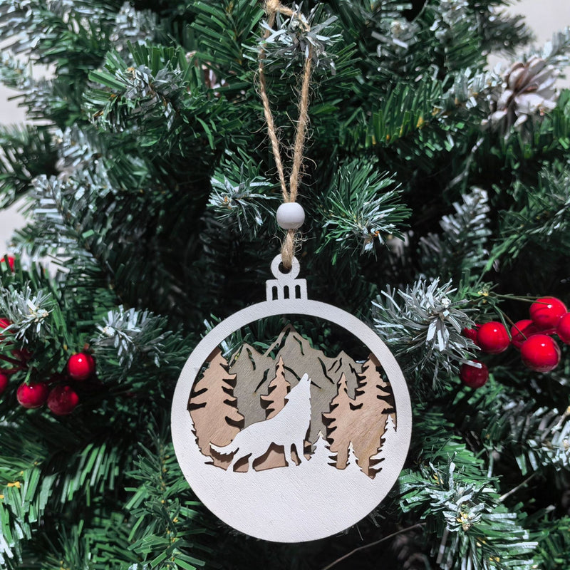 Decorative Christmas ornament with a wolf and mountain design hanging on a tree.
