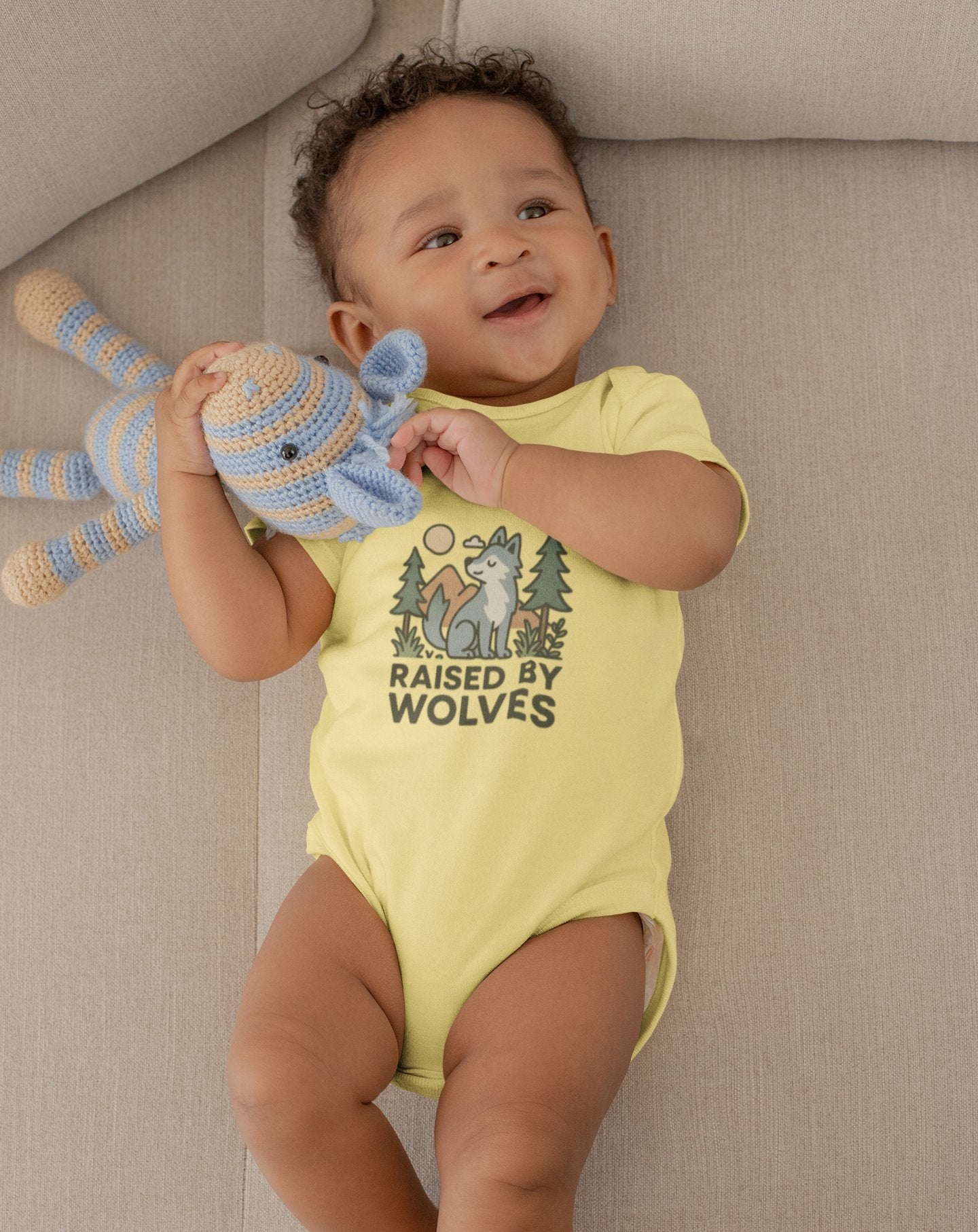 Baby wearing yellow onesie that says "Raised By Wolves" with a wolf graphic.