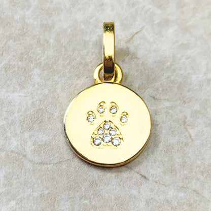 Gold pendant with paw print design on a beige stone surface