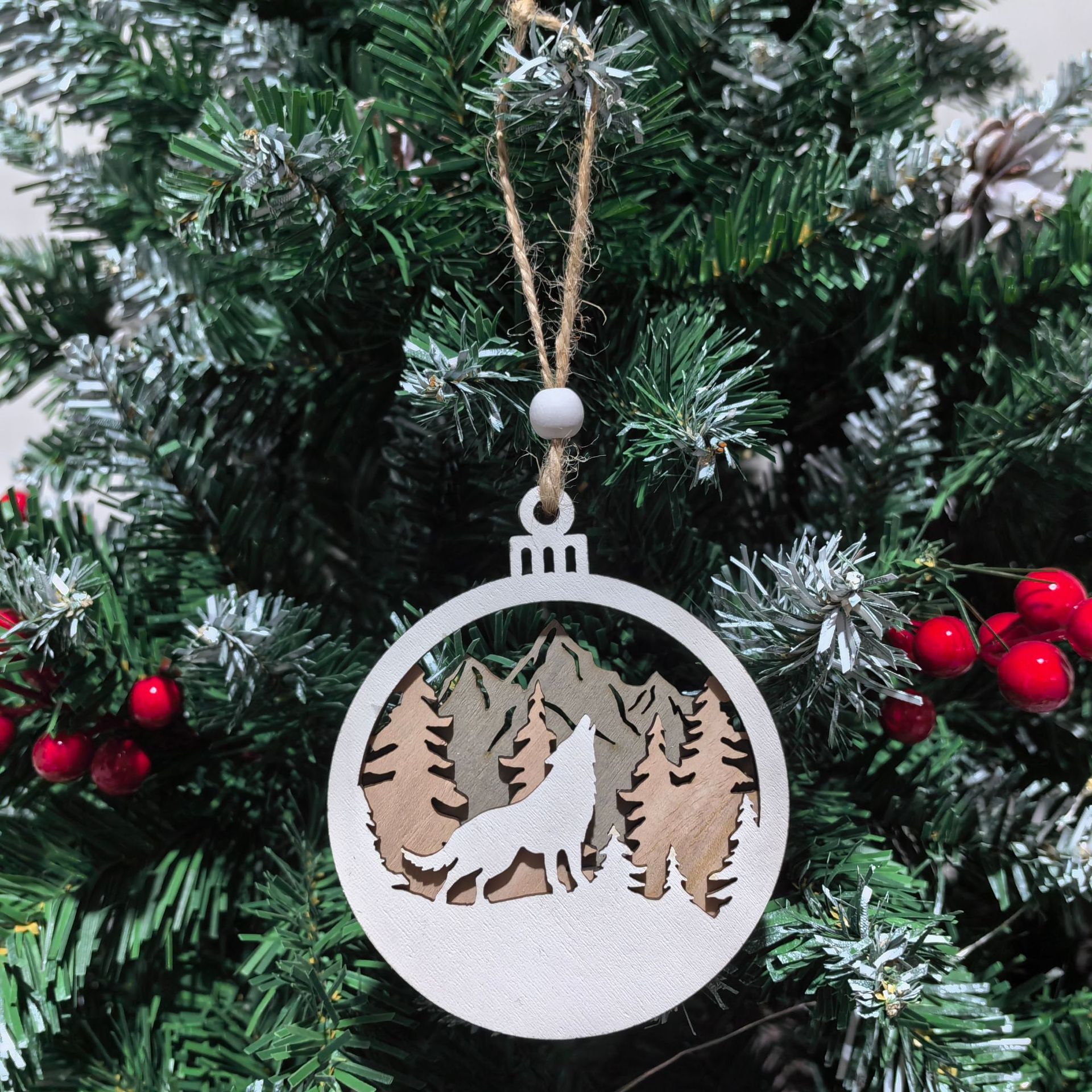 Decorative Christmas ornament with a wolf and mountain design hanging on a tree.
