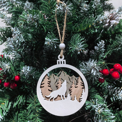 Decorative Christmas ornament with a wolf and mountain design hanging on a tree.